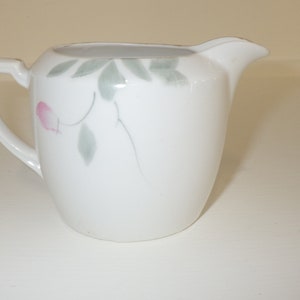 Puede incluir: Jarrita de cerámica blanca con un diseño floral en tonos rosa y verde.