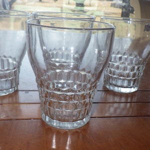 Könnte beinhalten: Vier klare Glasbecher mit einem strukturierten, diamantartigen Muster. Die Gläser stehen auf einem Holztisch.