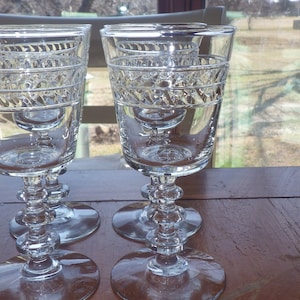 May include: Three clear glass wine goblets with a cut glass design. The goblets are on a wooden table.
