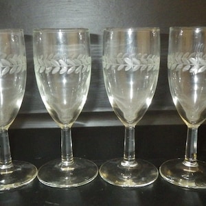 May include: Four clear wine glasses with an etched leaf pattern around the rim. Each glass has a slender stem and a circular base. The glasses are displayed in a row, suitable for serving wine.