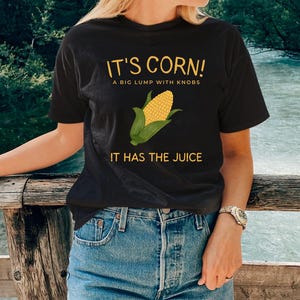 May include: A black t-shirt with a yellow corn graphic and the text "It's Corn! A big lump with knobs. It has the juice."