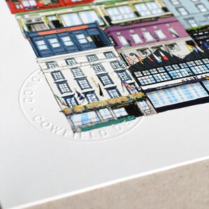 May include: A white background with a detailed illustration of a street scene in Dublin, Ireland. The illustration features multiple buildings, flags, and a stamp that reads "C100 - COWFIELD ST."