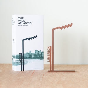 Może przedstawiać: Pudełko z tekstem "The Wild Atlantic Metal Model" i czarno-białym obrazem panoramy miasta. Obok pudełka znajduje się miedziany model metalowy panoramy miasta z napisem "Limerick".