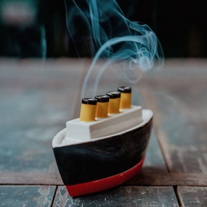Peut inclure: Un petit brûleur d'encens en forme de bateau noir et rouge avec quatre cheminées jaunes et noires. De la fumée s'échappe des cheminées.