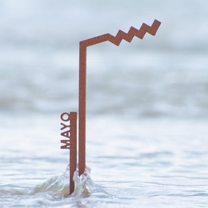 Puede incluir: Una escultura de metal oxidado en forma de llave con la palabra "MAYO" escrita verticalmente en el lateral. La escultura está parcialmente sumergida en el agua.