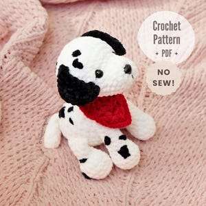 May include: A white and black spotted crochet dog plushie wearing a red bandana. The text on the image reads: Crochet Pattern PDF NO SEW! The plushie has black ears, black spots on its body, and black plastic eyes. It is a soft, stuffed toy.