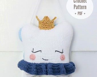 May include: A white crochet tooth plushie wearing a gold crown and a dark blue ruffled skirt. The tooth has embroidered closed eyes, a small smile, and pink cheeks. A white string is attached for hanging. Text reads: Crochet Pattern PDF.