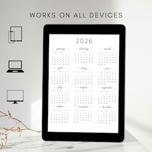 Op de afbeelding: Een digitale kalender voor het jaar 2026, weergegeven op een tablet. De kalender is in zwart-wit en toont alle 12 maanden van het jaar. De tablet ligt op een wit oppervlak met een klein takje witte bloemen.
