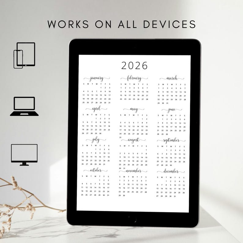 Op de afbeelding: Een digitale kalender voor het jaar 2026, weergegeven op een tablet. De kalender is in zwart-wit en toont alle 12 maanden van het jaar. De tablet ligt op een wit oppervlak met een klein takje witte bloemen.