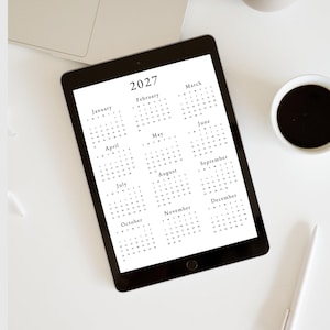 May include: A black tablet displaying a 2027 calendar with each month listed in a separate box. The months are January, February, March, April, May, June, July, August, September, October, November, and December.