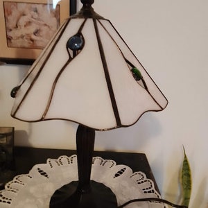 May include: A white stained glass lamp with a black metal base and three colored glass accents. The lamp is sitting on a white doily.