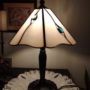 May include: A white stained glass table lamp with a black metal base and a white shade. The lamp has three blue glass accents on the shade.