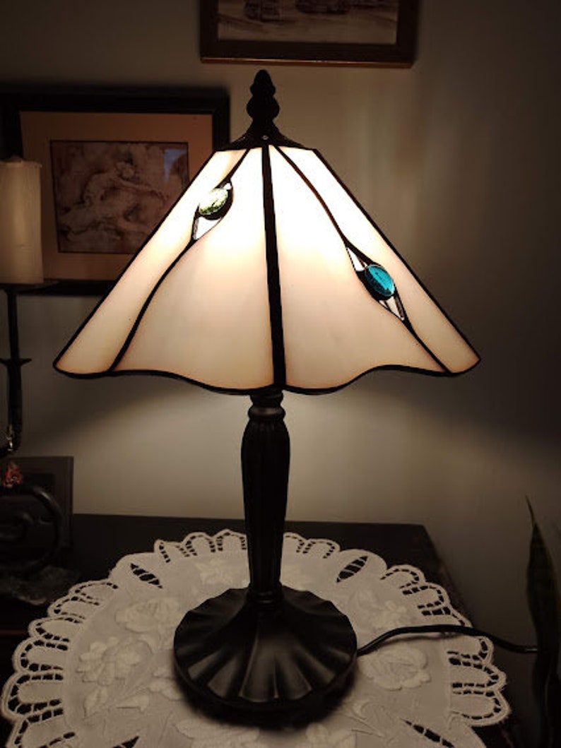 May include: A white stained glass table lamp with a black metal base and a white shade. The lamp has three blue glass accents on the shade.