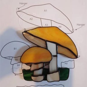 May include: A stained glass pattern for a Caesar's Mushroom. The pattern includes 12 pieces of glass, labelled A1 through A6, B1 through B5, and C1. The pattern is for a mushroom with a yellow cap and a white stem.
