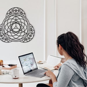 Puede incluir: Una mujer se sienta en una mesa con un port&aacute;til, un libro y una taza. Una pieza de arte geom&eacute;trico de pared cuelga en la pared detr&aacute;s de ella.