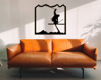 Op de afbeelding: Zwarte metalen wandkunst met een silhouet van een skiër die een truc uitvoert tegen een bergachtergrond.