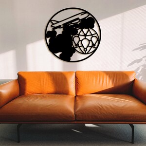 May include: Black metal wall art depicting an aeroplane flying over a globe with hot air balloons. The art is mounted on a white wall above a brown leather sofa.