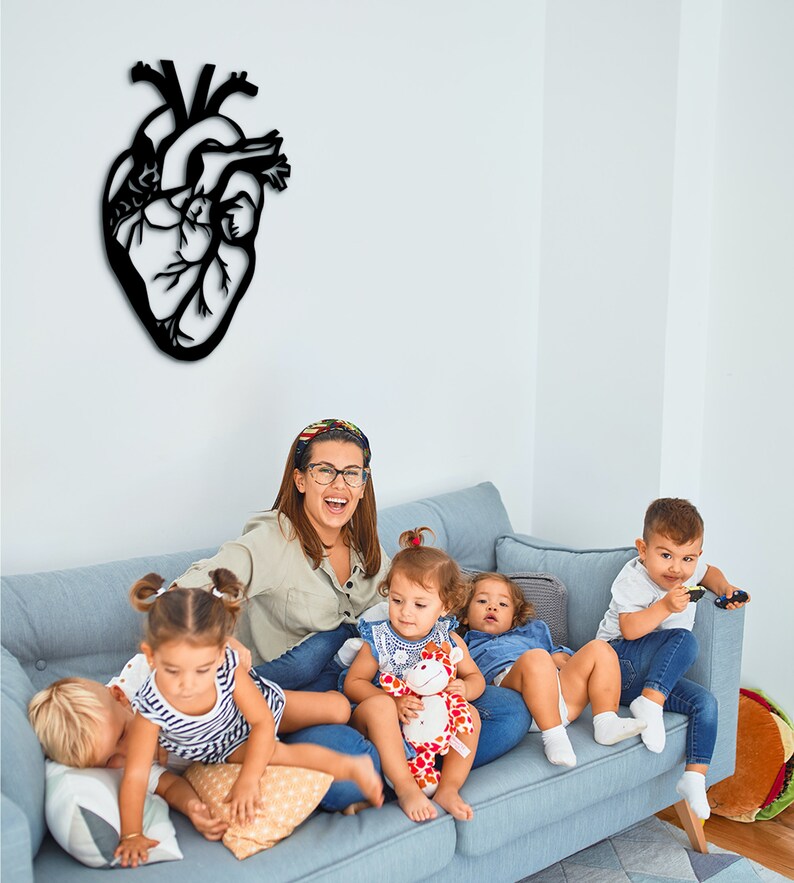 Op de afbeelding: Een groep kinderen en een volwassene zitten op een blauwe bank. De volwassene draagt een lichtblauw shirt en een bril. De kinderen dragen verschillende kleding. Er is een zwarte hartvormige wanddecoratie op de muur achter de bank.