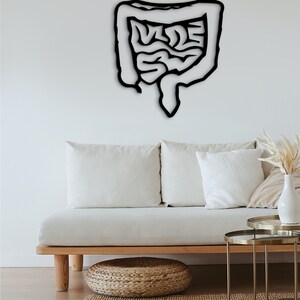 May include: Black metal wall art depicting a human intestine. The art is mounted on a white wall above a white couch with wooden legs.