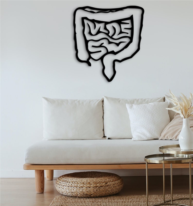 May include: Black metal wall art depicting a human intestine. The art is mounted on a white wall above a white couch with wooden legs.