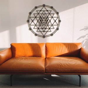 May include: A brown leather sofa with a black metal frame sits in front of a white wall with a black geometric design on it. The design is a circle with a series of triangles and lines inside.