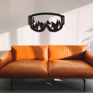 May include: Black metal wall art in the shape of ski goggles with a mountain and pine tree design.