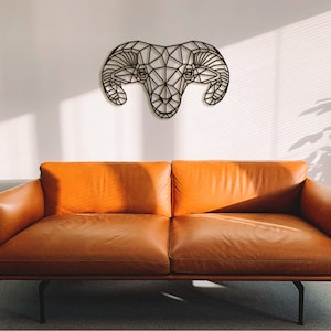 May include: A black geometric ram head wall decor hangs above a brown leather sofa in a modern living room.