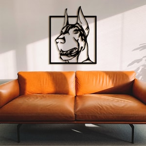 May include: Black metal wall art featuring a Doberman Pinscher dog head silhouette in a square frame. The art is mounted on a white wall above a brown leather sofa.