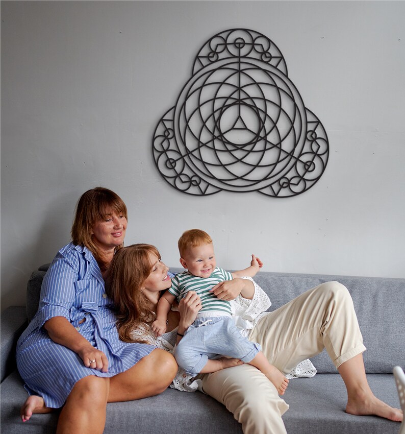 Puede incluir: Dos adultos y un ni&ntilde;o est&aacute;n sentados en un sof&aacute; gris frente a una pieza de arte de pared geom&eacute;trica negra. Los adultos est&aacute;n sonriendo y el ni&ntilde;o est&aacute; riendo. Los adultos visten ropa casual y el ni&ntilde;o lleva una camisa a rayas verde y blanca y pantalones vaqueros azules.