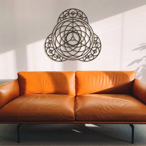 Puede incluir: Un sof&aacute; de cuero marr&oacute;n con un marco de metal negro se encuentra frente a una pared blanca con una pieza de arte de pared de metal geom&eacute;trico colgada encima.