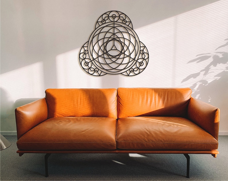 Puede incluir: Un sof&aacute; de cuero marr&oacute;n con un marco de metal negro se encuentra frente a una pared blanca con una pieza de arte de pared de metal geom&eacute;trico colgada encima.