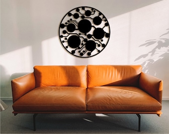 Könnte beinhalten: Eine schwarze Wanddekoration aus Metall in Form eines Kreises mit einem geometrischen Muster aus Linien und Kreisen. Die Dekoration hängt an einer weißen Wand über einem braunen Ledersofa.