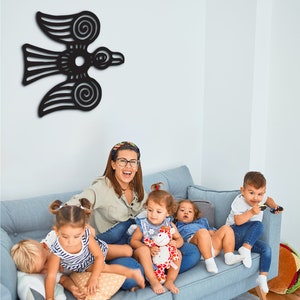 May include: A woman and four children sit on a light blue couch. The woman is wearing a light blue shirt and glasses. The children are wearing various colorful clothing. A black bird wall decor hangs on the wall behind them.