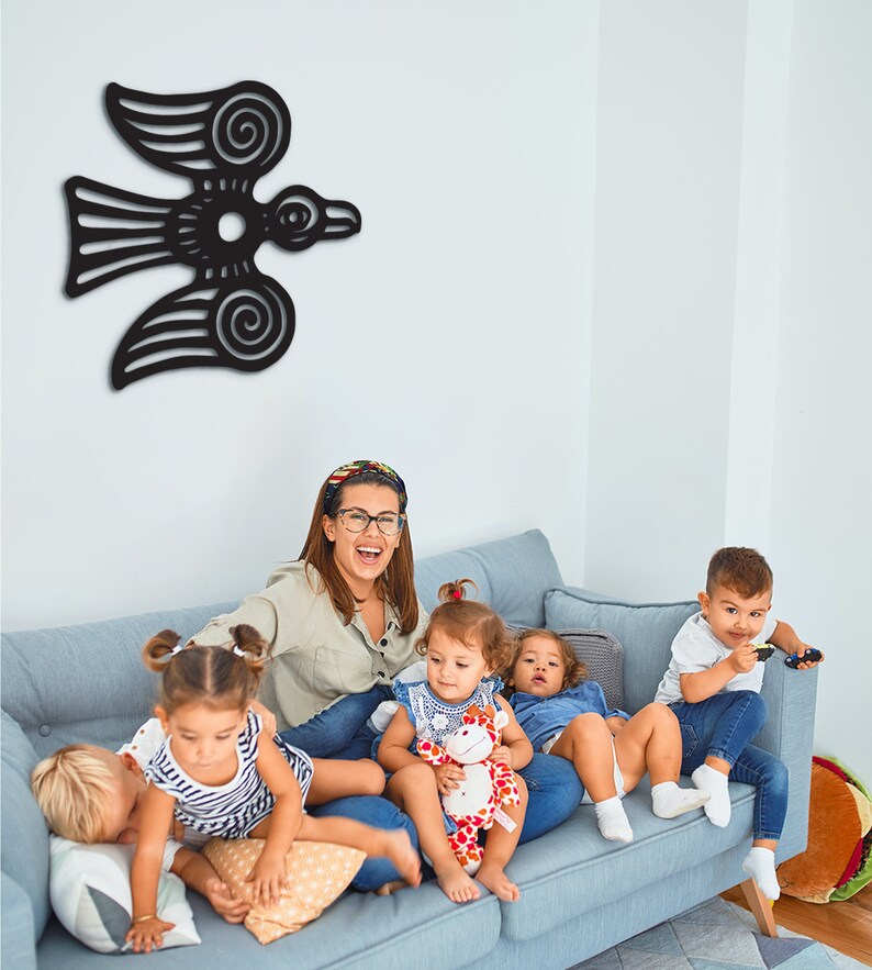 May include: A woman and four children sit on a light blue couch. The woman is wearing a light blue shirt and glasses. The children are wearing various colorful clothing. A black bird wall decor hangs on the wall behind them.
