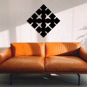 Puede incluir: Una pieza de arte de pared geométrica negra en forma de diamante con un patrón repetitivo de cuadrados y círculos. El arte está colgado en una pared blanca sobre un sofá de cuero marrón.