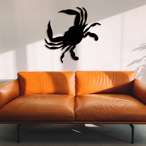 May include: A black metal silhouette of a crab mounted on a white wall above a brown leather couch.