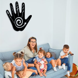 May include: A group of children and an adult are sitting on a blue couch. The children are playing with toys. There is a black handprint with a spiral design on the wall behind them.