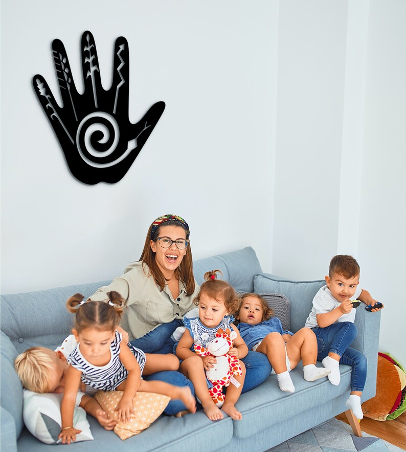 May include: A group of children and an adult are sitting on a blue couch. The children are playing with toys. There is a black handprint with a spiral design on the wall behind them.