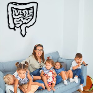 May include: A woman and four children sit on a blue couch. The woman is wearing a light brown shirt and glasses. The children are playing with toys. A black and white drawing of a human digestive system is on the wall behind them.
