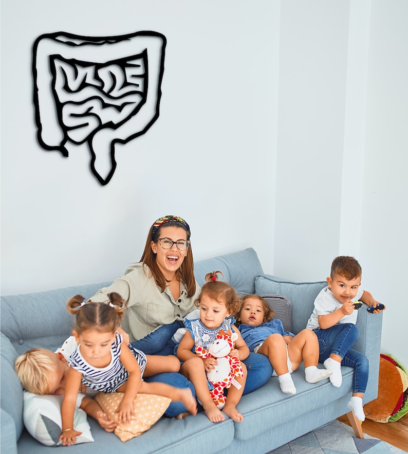 May include: A woman and four children sit on a blue couch. The woman is wearing a light brown shirt and glasses. The children are playing with toys. A black and white drawing of a human digestive system is on the wall behind them.