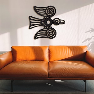 May include: A black metal wall art sculpture of a stylized bird with intricate details. The sculpture is mounted on a white wall above a brown leather couch.