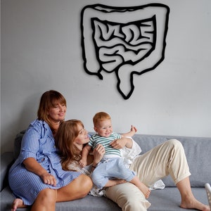 May include: Two adults and a child sitting on a gray couch. The adults are smiling and the child is looking at the camera. There is a black outline of a human intestine on the wall behind them.