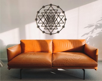 May include: A black metal wall decor featuring a geometric design with a circular frame. The decor is hanging on a white wall above a brown leather couch.