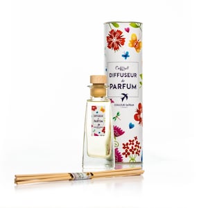 Op de afbeelding: Een diffuserset met een heldere glazen fles en een kleurrijk bloemenontwerp op de doos. De doos heeft de tekst "Coffret Diffuseur de Parfum" en "Couleur Safran Cannes".