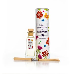 Könnte beinhalten: Ein Duftdiffusor-Set mit einer transparenten Glasflasche, einem Holzstopfen und Stäbchen. Die Flasche hat ein Etikett mit Text und floralen Designs. Ein zylindrischer Behälter mit bunten Blumen und Schmetterlingen befindet sich hinter der Flasche.