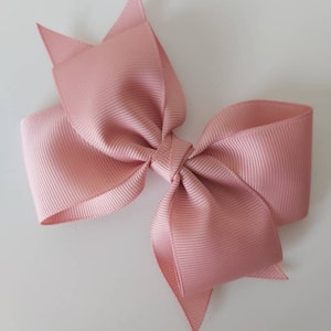 May include: A large, blush pink bow made from grosgrain ribbon. The bow is tied in a classic style with two loops and two tails.