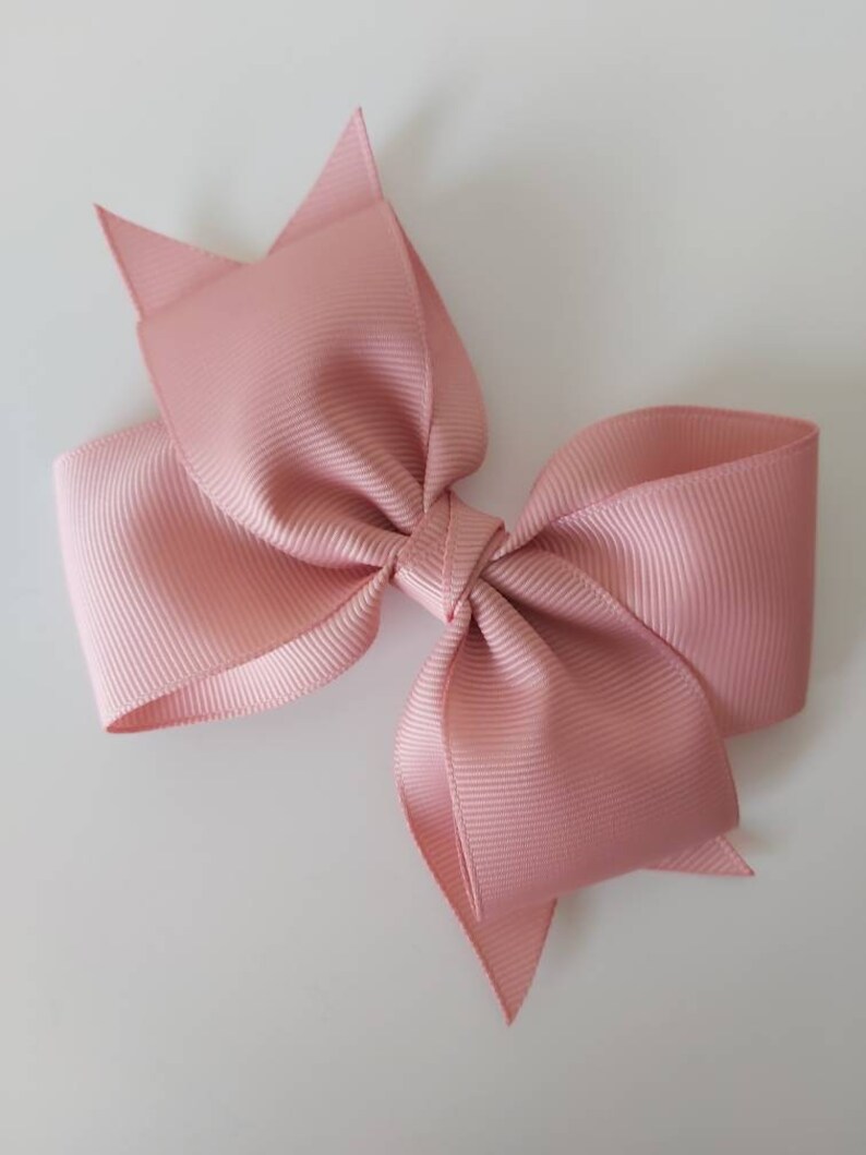 May include: A large, blush pink bow made from grosgrain ribbon. The bow is tied in a classic style with two loops and two tails.