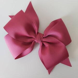 May include: A large, pink satin bow with a textured finish. The bow is tied in a classic shape with two loops and a centre knot.