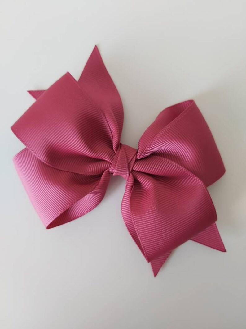 May include: A large, pink satin bow with a textured finish. The bow is tied in a classic shape with two loops and a centre knot.