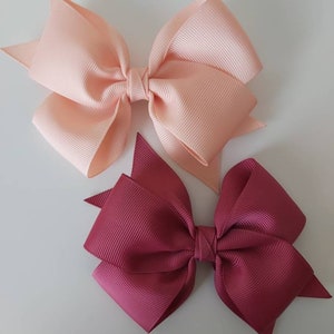 May include: Two hair bows, one peach and one burgundy, made of grosgrain ribbon. The bows are tied with a knot in the centre and have a pointed shape at the ends.